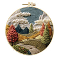 Complete DIY embroidery kit showing pre-printed landscape fabric, coloured threads, needles, and an embroidery frame.