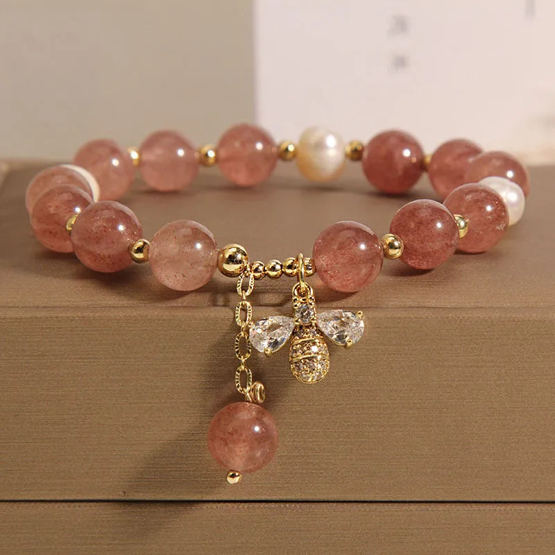 Close-up of a women's bracelet with pink strawberry quartz beads, white freshwater pearls, and sparkling zircon charms on an alloy chain.