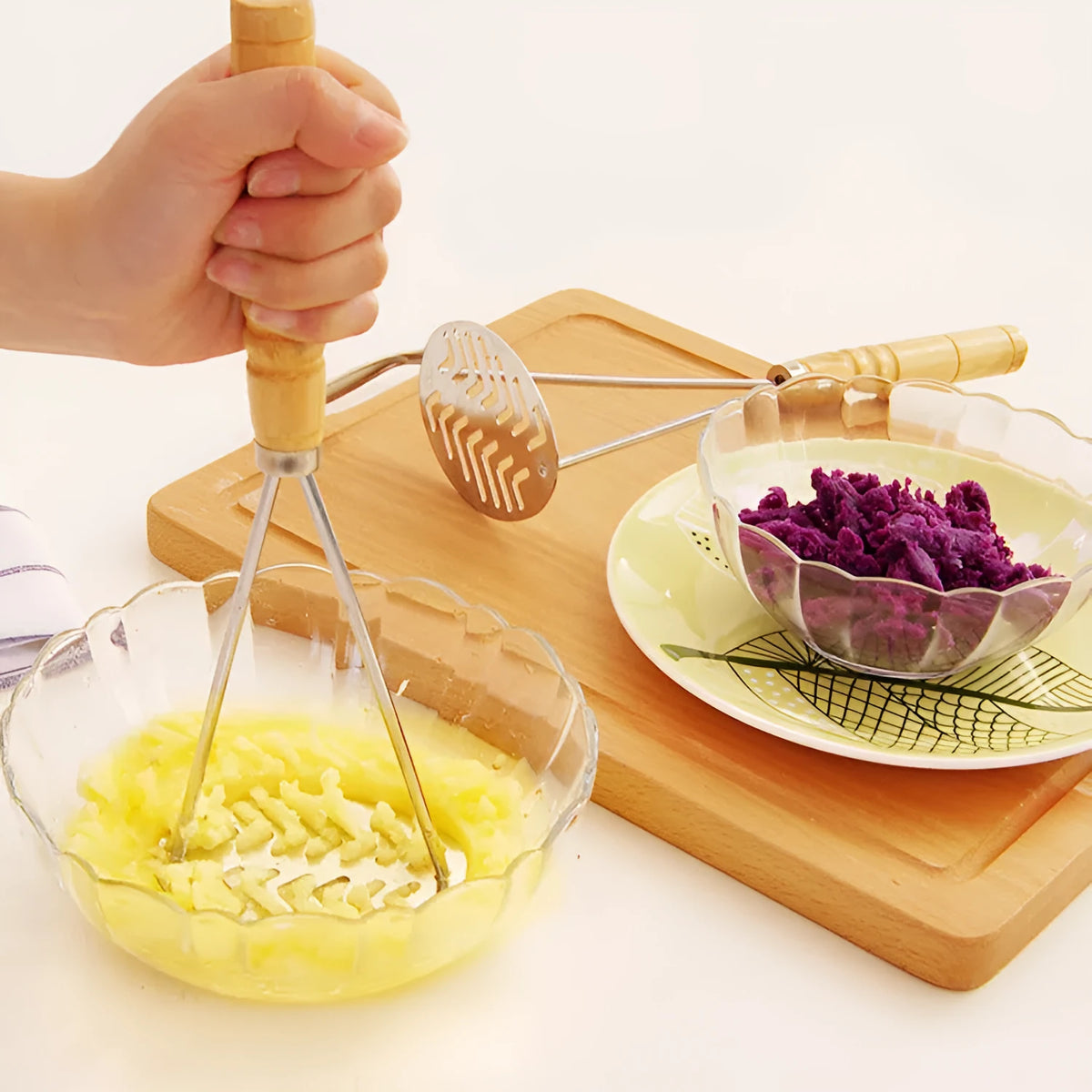 Manual potato masher with wooden handle and flower-shaped iron plated press head on a light surface