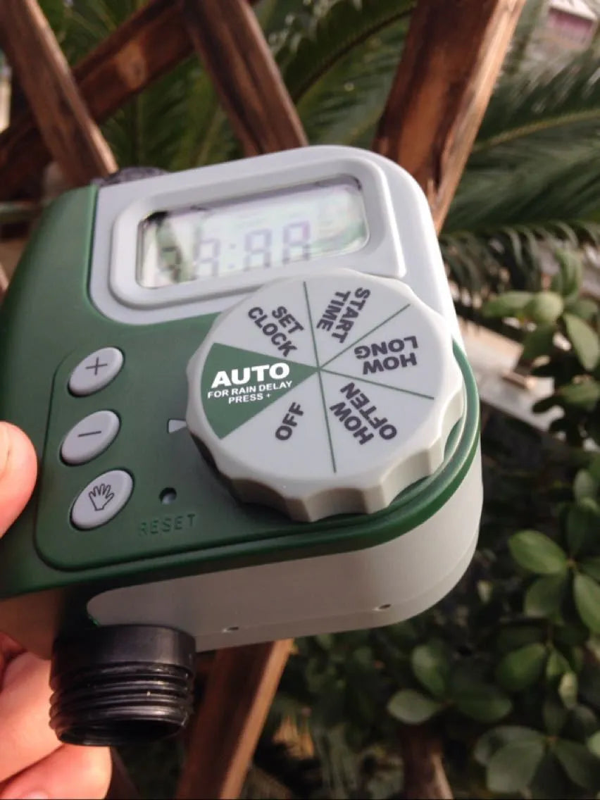 Green digital programmable water timer with display and dial attached to a garden hose faucet.