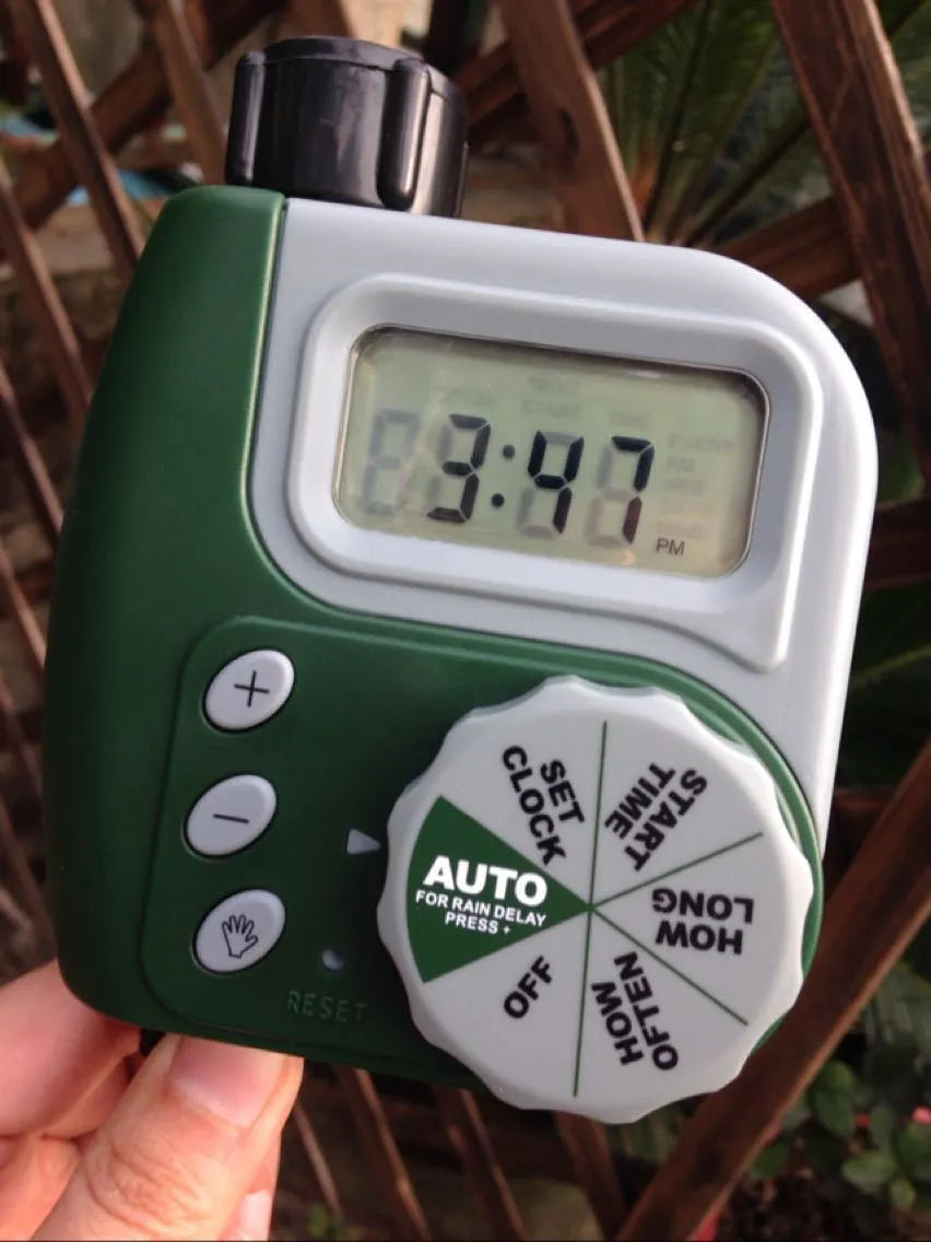 Green digital programmable water timer with display and dial attached to a garden hose faucet.
