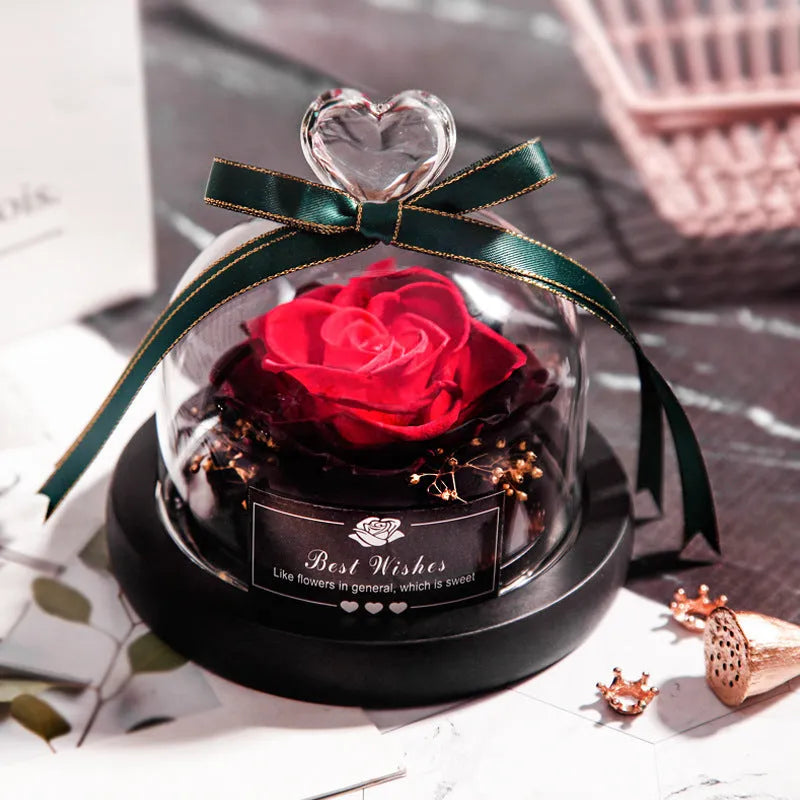 Eternal preserved red rose illuminated by LED light inside a clear glass dome on a wooden table.