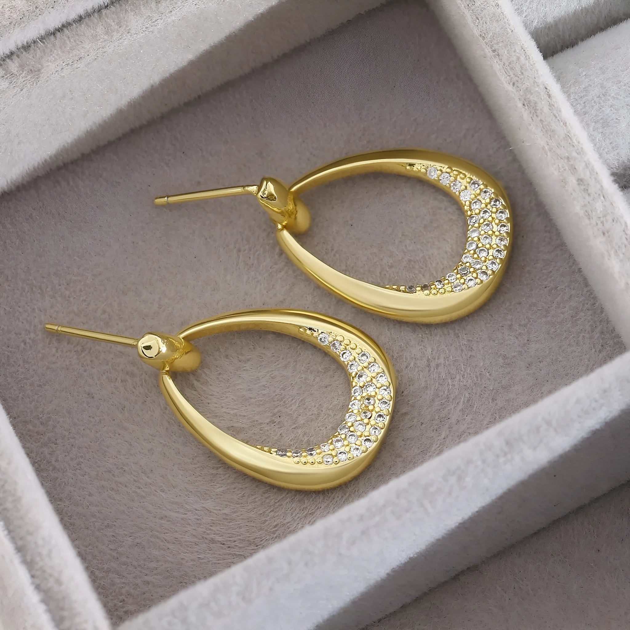 Yellow gold geometric drop-shaped women's earrings with round and oval ring elements on a simple background.