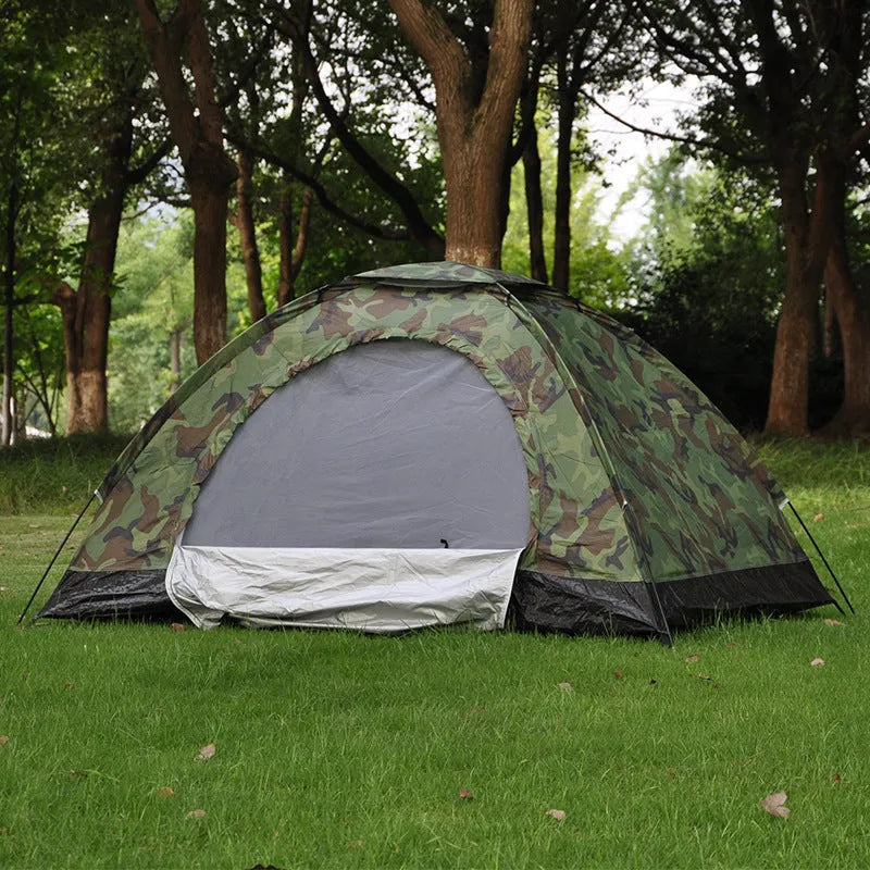 Green camouflage two-person camping tent with fibre glass poles and steel pegs pitched outdoors.