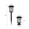 Black solar-powered outdoor LED lawn light with window-style openings, shown in a garden setting.