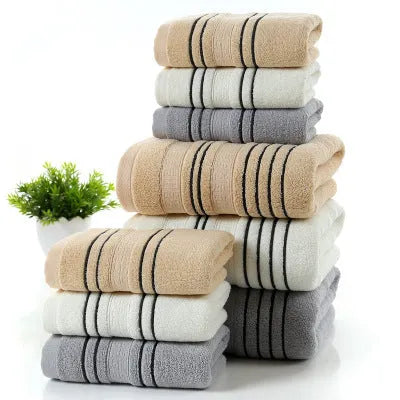 Set of one white 70x140cm cotton bath towel and two smaller grey hand towels on a bathroom shelf.