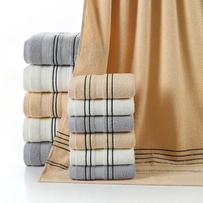 Set of one white 70x140cm cotton bath towel and two smaller grey hand towels on a bathroom shelf.