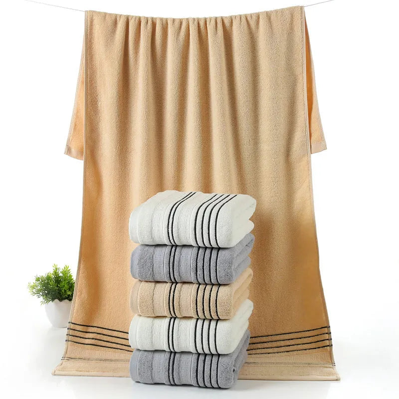 Set of one white 70x140cm cotton bath towel and two smaller grey hand towels on a bathroom shelf.
