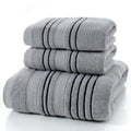 Set of one white 70x140cm cotton bath towel and two smaller grey hand towels on a bathroom shelf.
