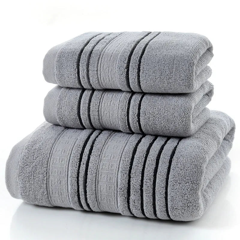 Set of one white 70x140cm cotton bath towel and two smaller grey hand towels on a bathroom shelf.