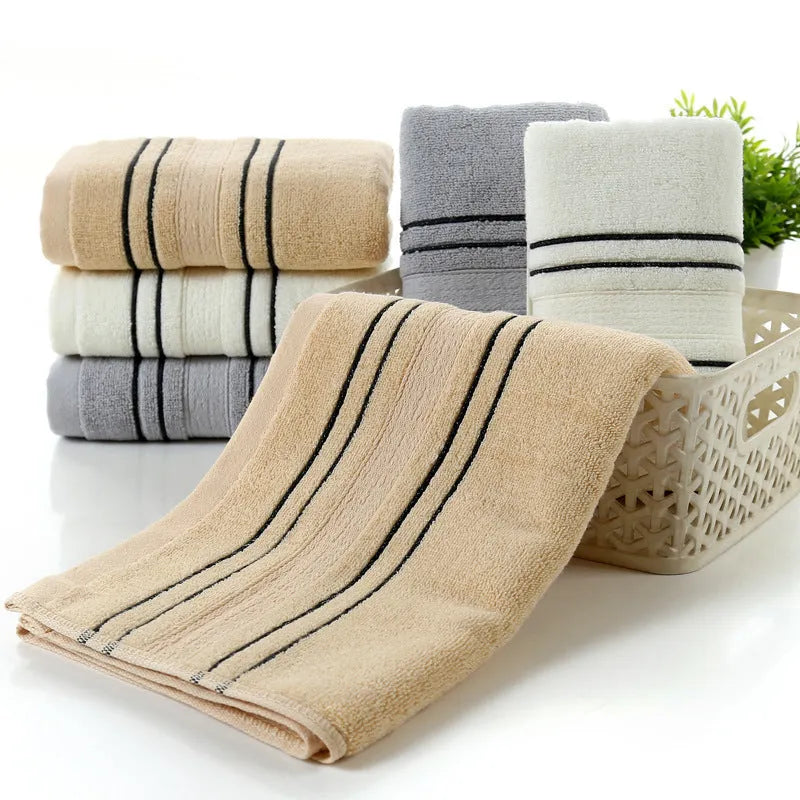 Set of one white 70x140cm cotton bath towel and two smaller grey hand towels on a bathroom shelf.