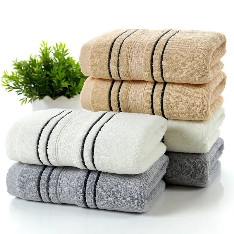 Set of one white 70x140cm cotton bath towel and two smaller grey hand towels on a bathroom shelf.