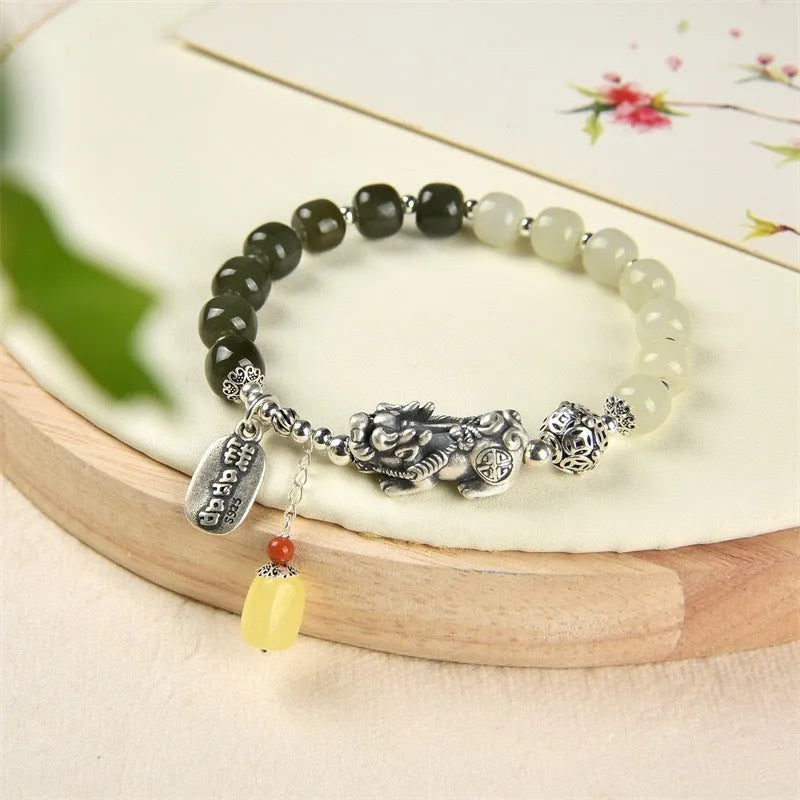 Close-up of a retro women's bracelet with a natural Hetian jade bead and a silver coin pendant on a wrist.