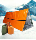 Orange emergency survival blanket unfolded showing reflective inner surface, with folded sleeping bag and tent beside it in nylon bag