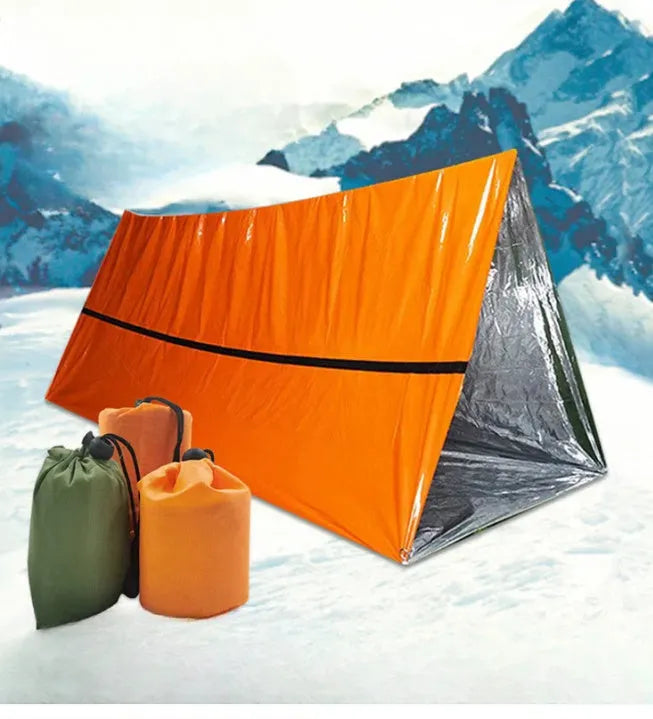 Orange emergency survival blanket unfolded showing reflective inner surface, with folded sleeping bag and tent beside it in nylon bag