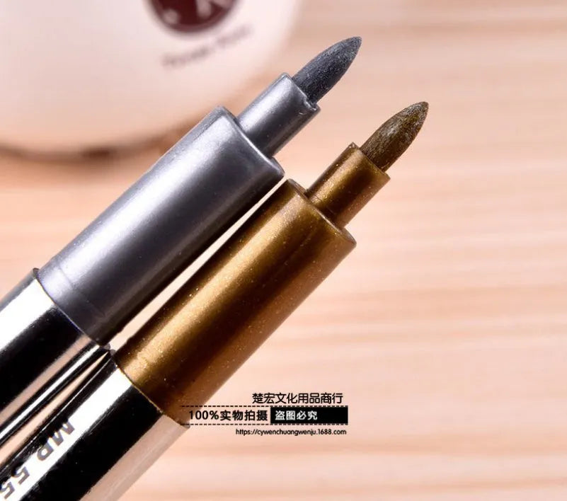 Gold and silver metallic marker pen set with dual tips lying on a white surface