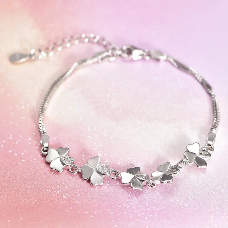Silver four-leaf clover bracelet with leaf pendant on a plain background