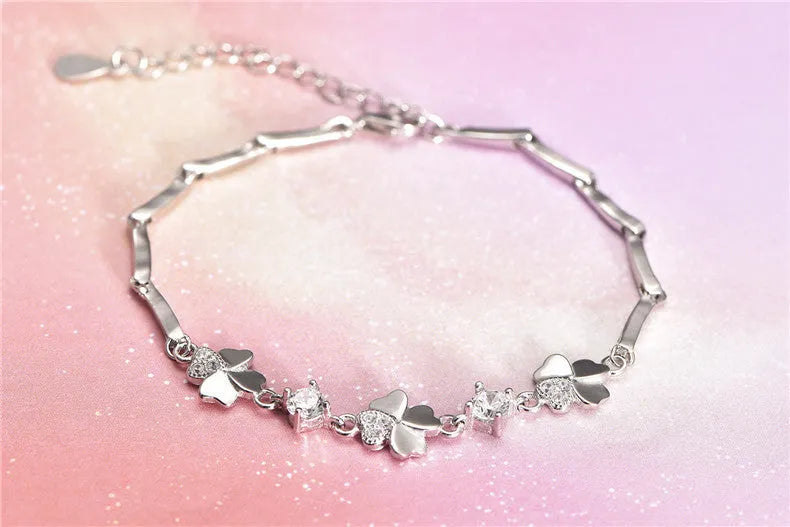 Silver four-leaf clover bracelet with leaf pendant on a plain background