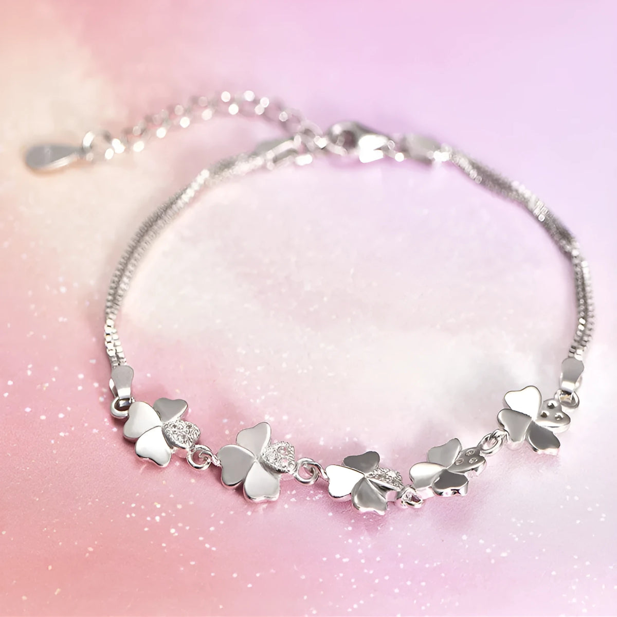 Silver four-leaf clover bracelet with leaf pendant on a plain background