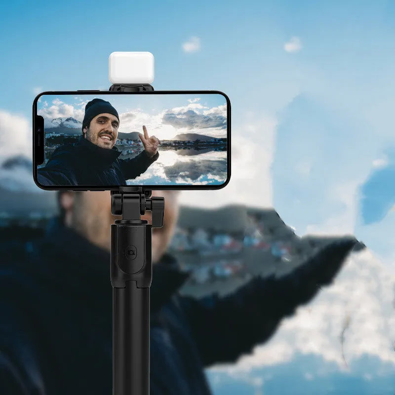 Black Bluetooth selfie stick tripod with fill light extended, holding a smartphone.