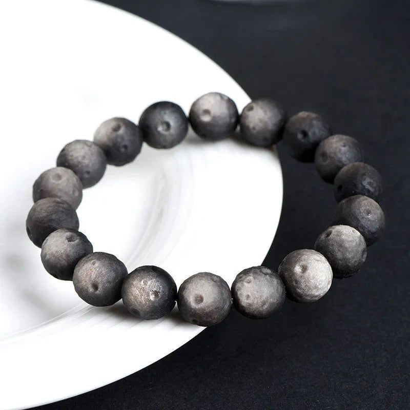Natural obsidian crater ball bracelet with a ground texture in silver stone or gold colours on a wrist.