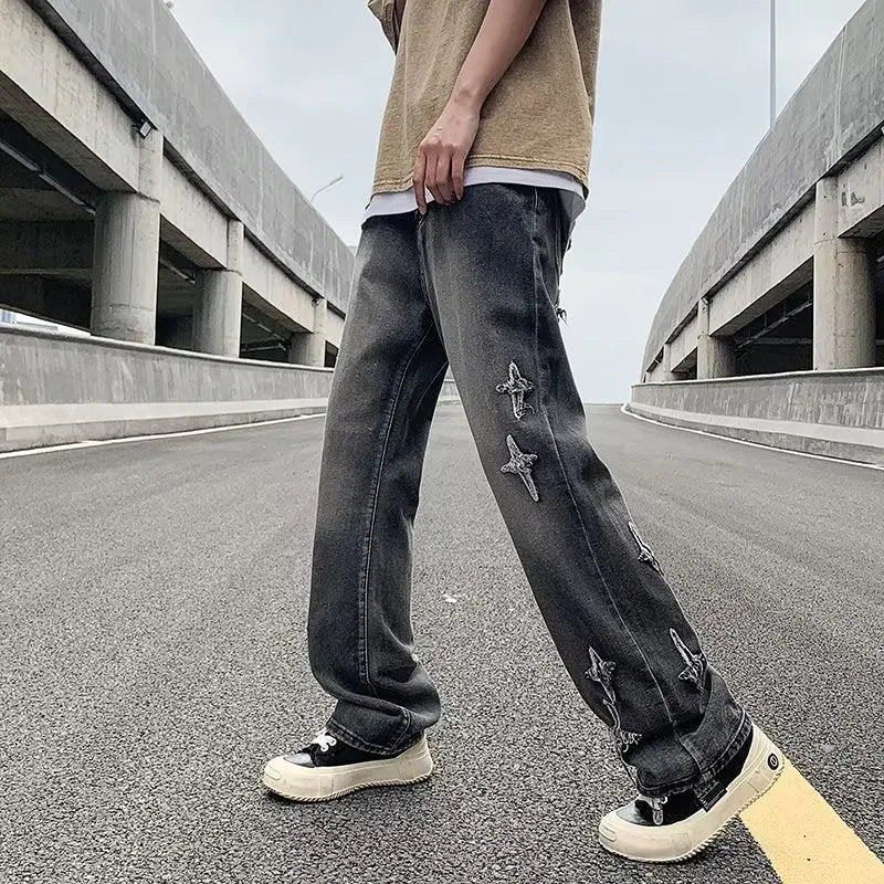 Men's loose denim trousers in black, straight-leg style with zipper fly, lying flat on a surface