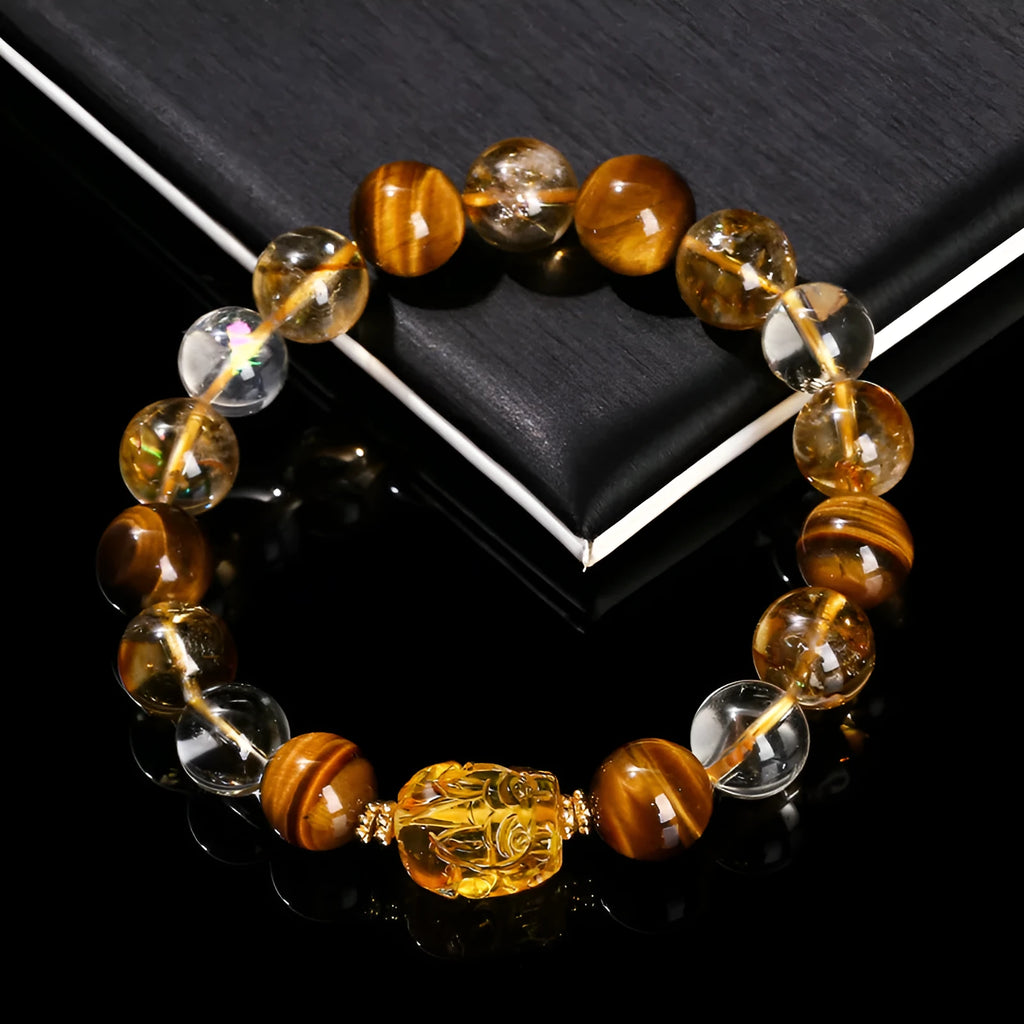 A close-up of a beaded bracelet with yellow banded Tiger's Eye and translucent citrine 10mm beads and a metallic Pi Xiu charm.