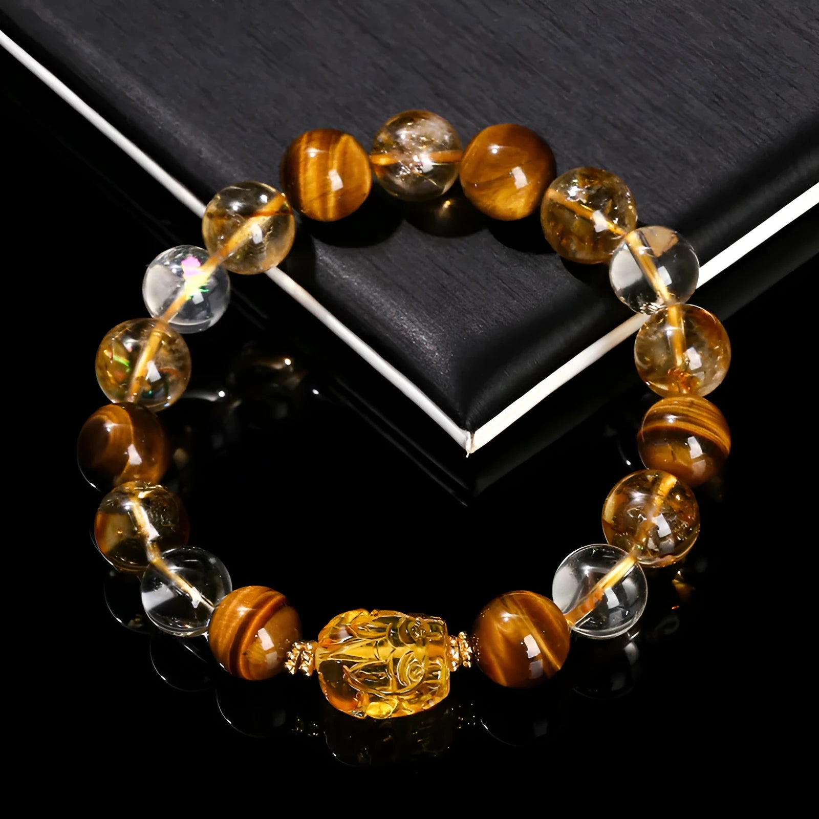 A close-up of a beaded bracelet with yellow banded Tiger's Eye and translucent citrine 10mm beads and a metallic Pi Xiu charm.