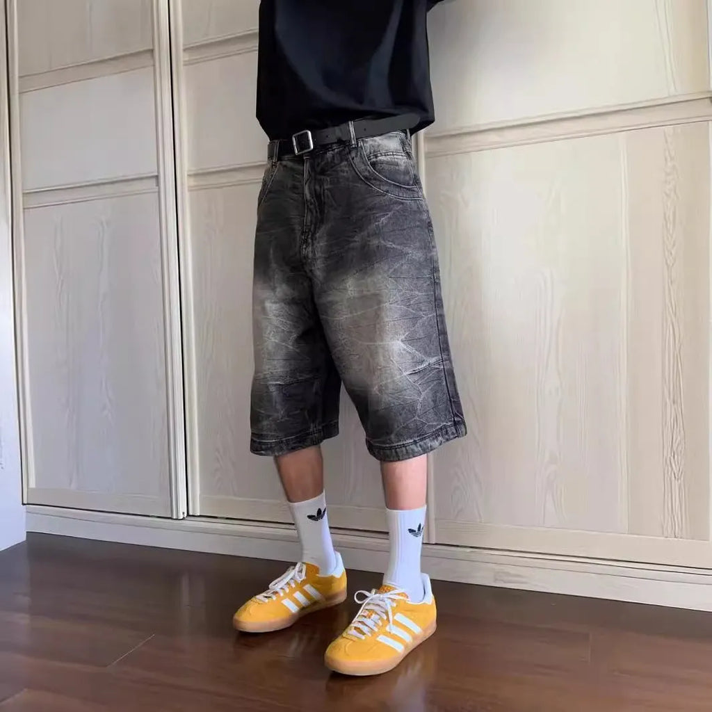 Man wearing loose straight-leg washed denim shorts in blue, showing cropped length and casual style.