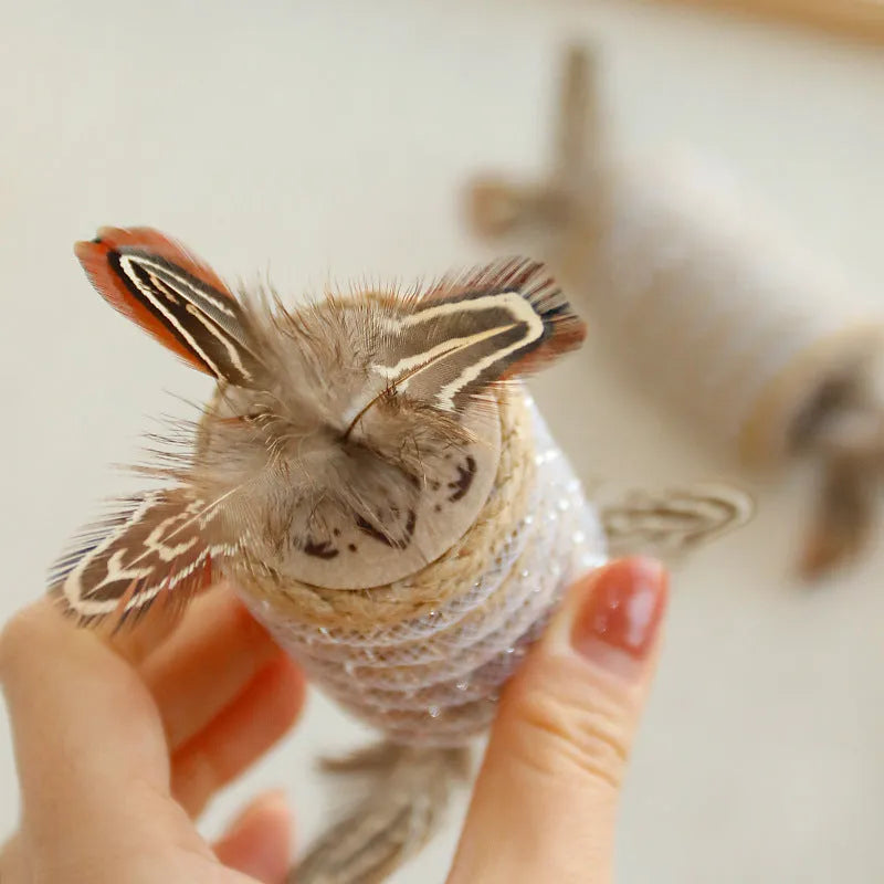 Beige cat toy with hemp rope scratching surface, attached feathers, and a roller for claw grinding.