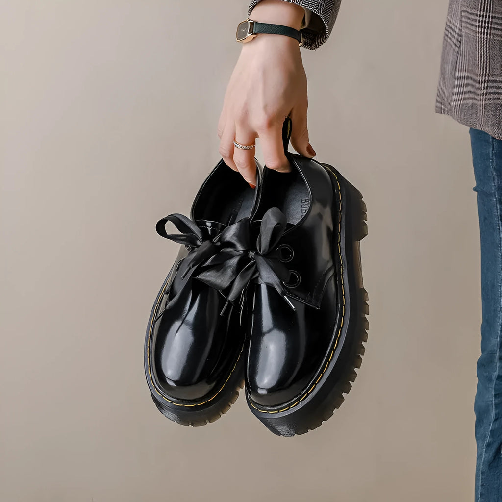 Black thick-soled women's leather shoes with cross-strap ribbons and lace-up closure on a white background.
