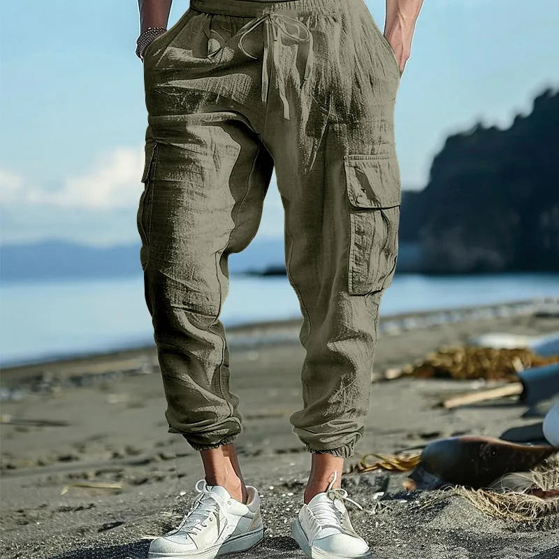 Man wearing loose khaki linen trousers with ankle-tied cuffs, drawstring waist, and multiple pockets.
