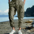Man wearing loose khaki linen trousers with ankle-tied cuffs, drawstring waist, and multiple pockets.