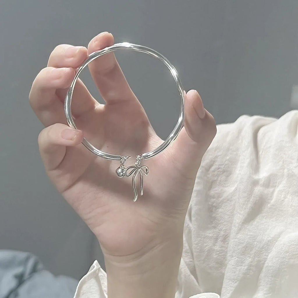Silver adjustable bow bracelet with a bell opening clasp on a wrist.