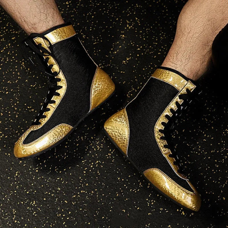 Pair of black and gold professional boxing shoes with mesh panels on a gym floor.