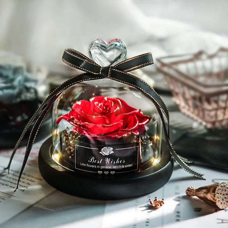Eternal preserved red rose illuminated by LED light inside a clear glass dome on a wooden table.