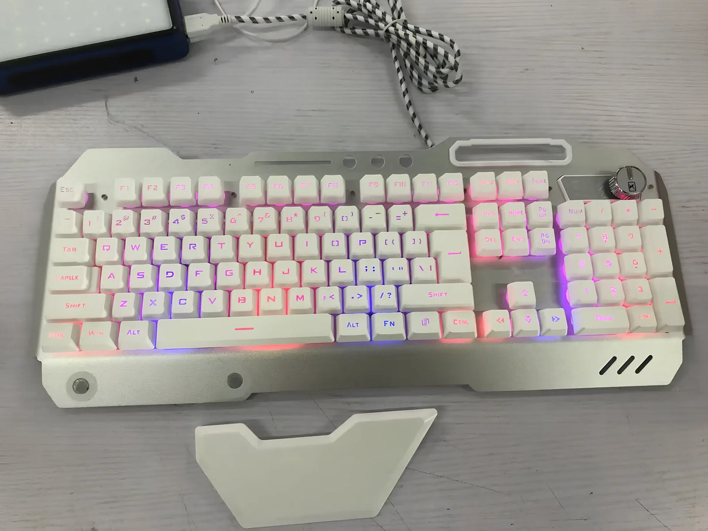 Black wired gaming keyboard with RGB backlight, phone holder, and magnetic wrist rest on desk