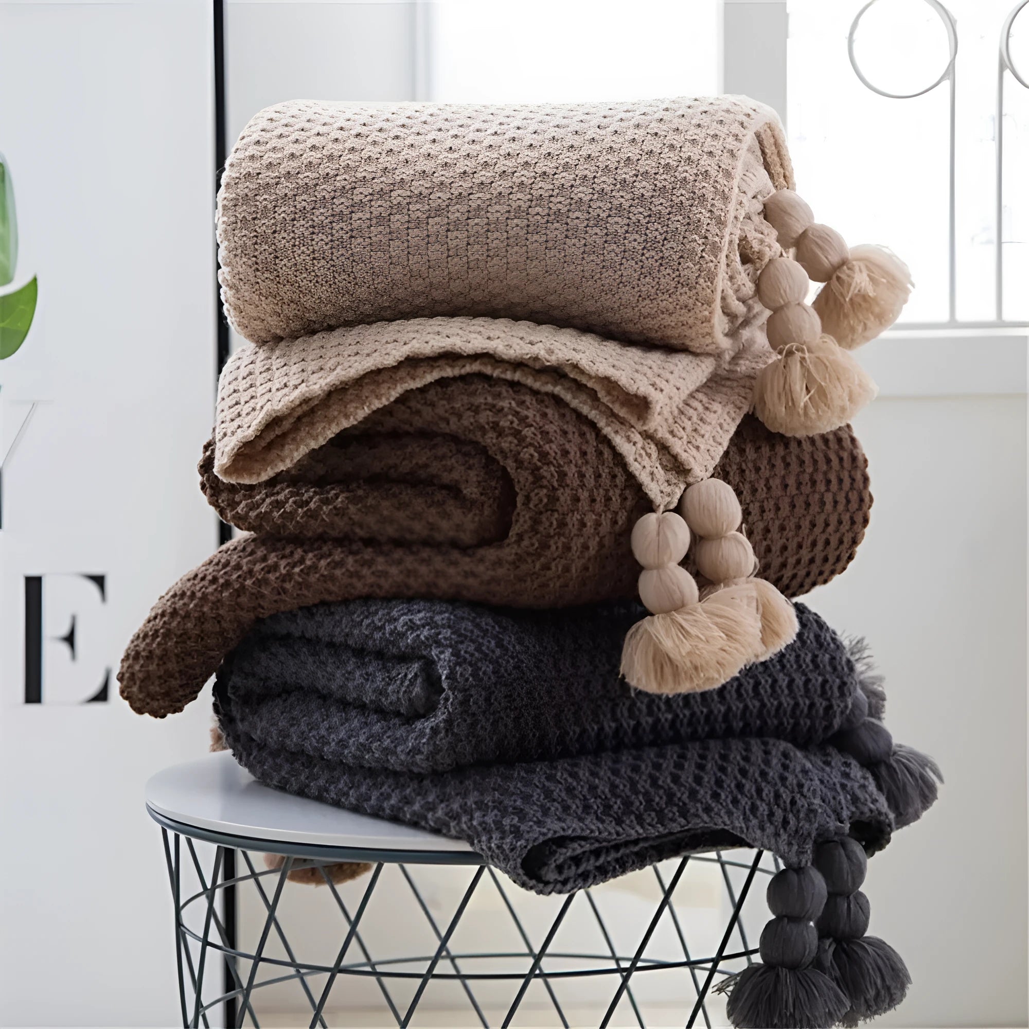 Nordic-style fringed knit acrylic blanket in a neutral colour, shown on a sofa.