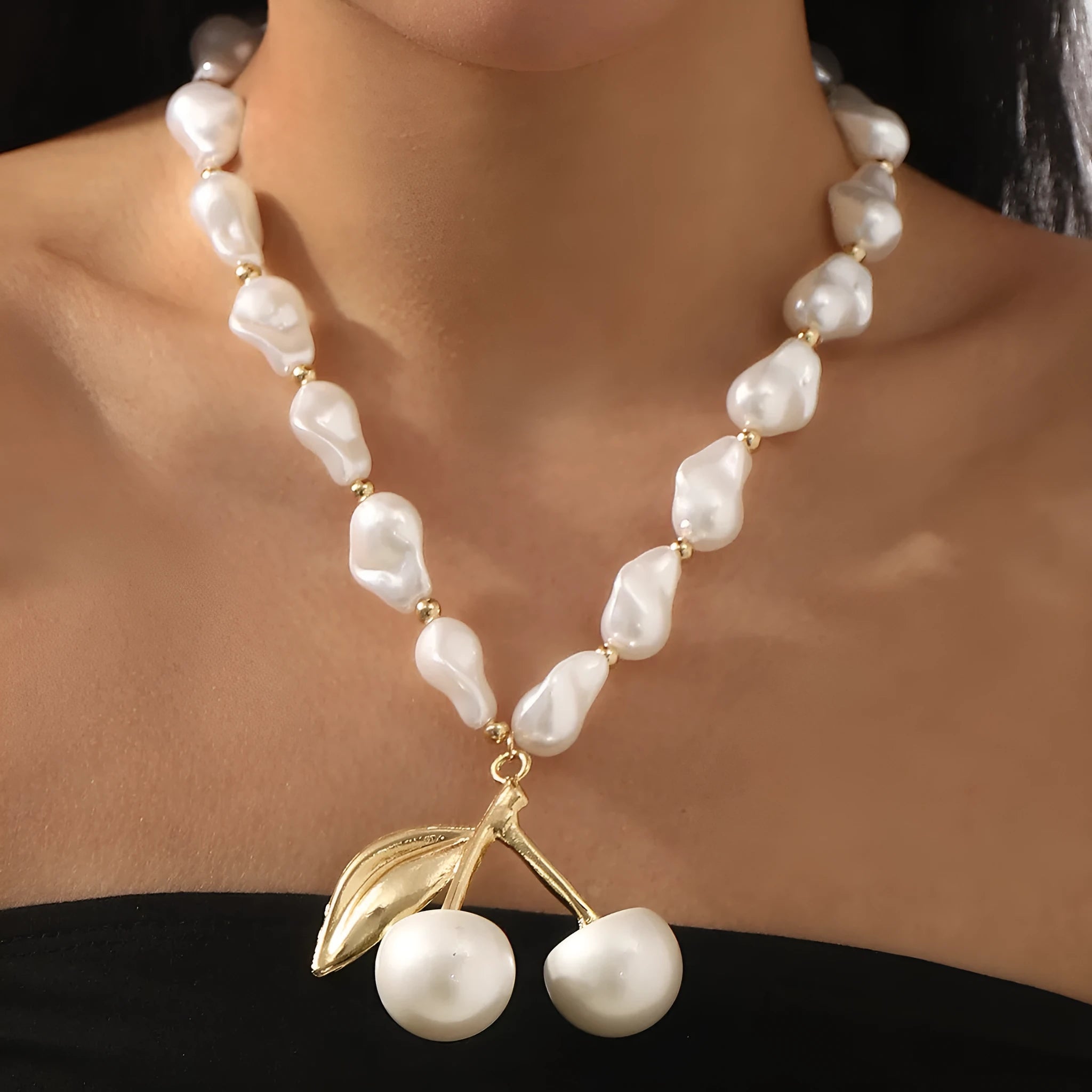 Gold-coloured women's necklace with a cherry fruit pendant on a pearl-style chain.