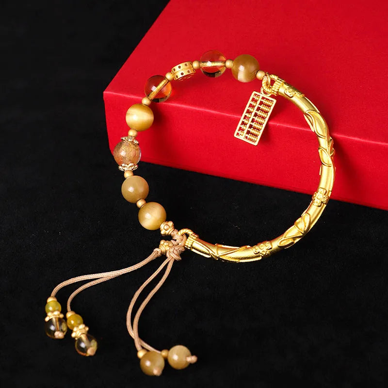 Close-up of a women's beaded bracelet with a diamond-shaped abacus tag bead, tigereye, citrine, and yellow tower crystal stones on copper.