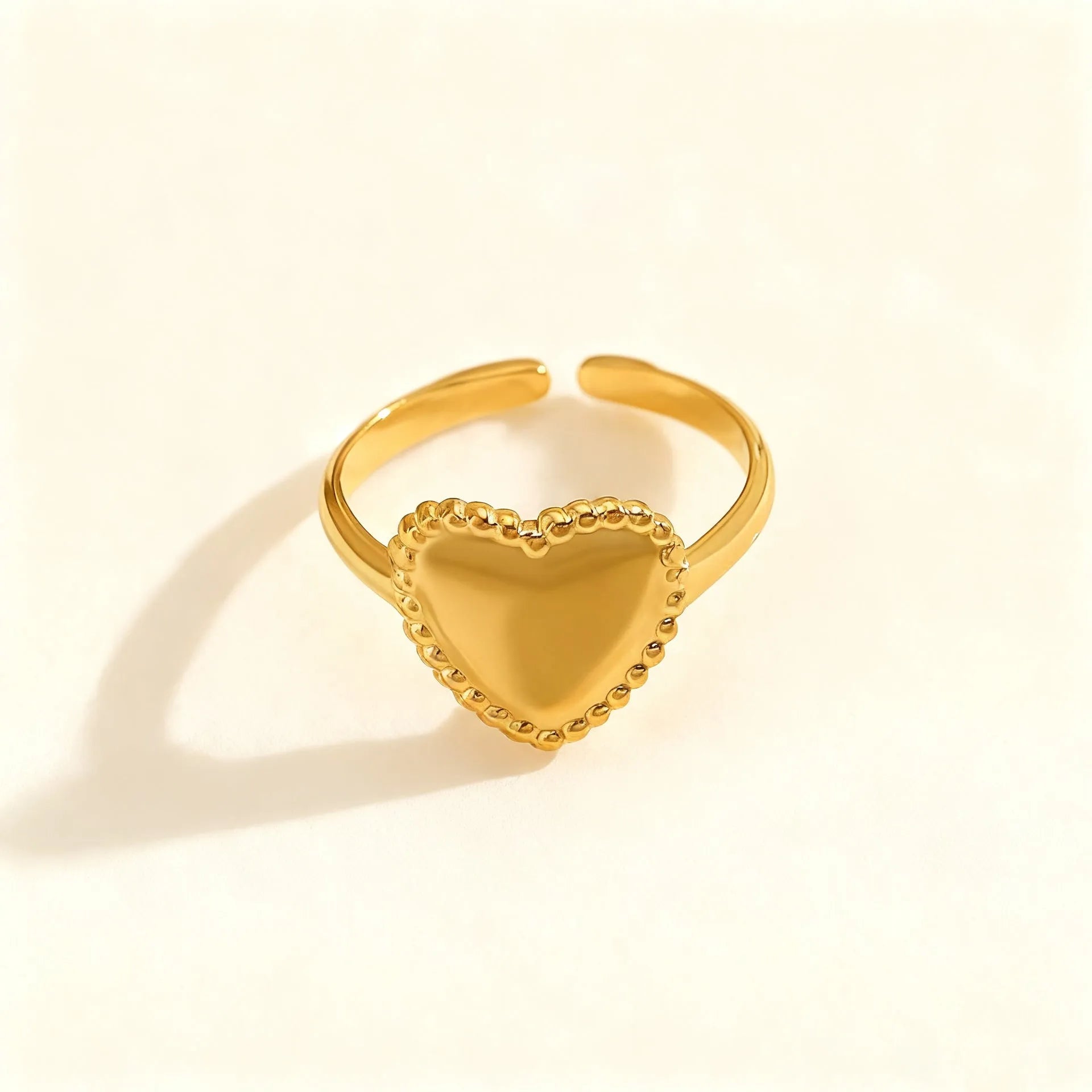 Adjustable stainless steel heart ring with electroplated gold finish on plain background