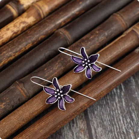 A pair of retro-style purple flower-shaped alloy earrings for women on a plain background.
