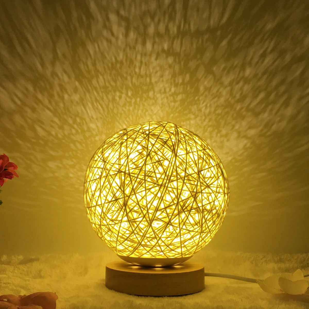 Hand-knit linen rattan ball table lamp with USB cable in blue colour on a wooden table.