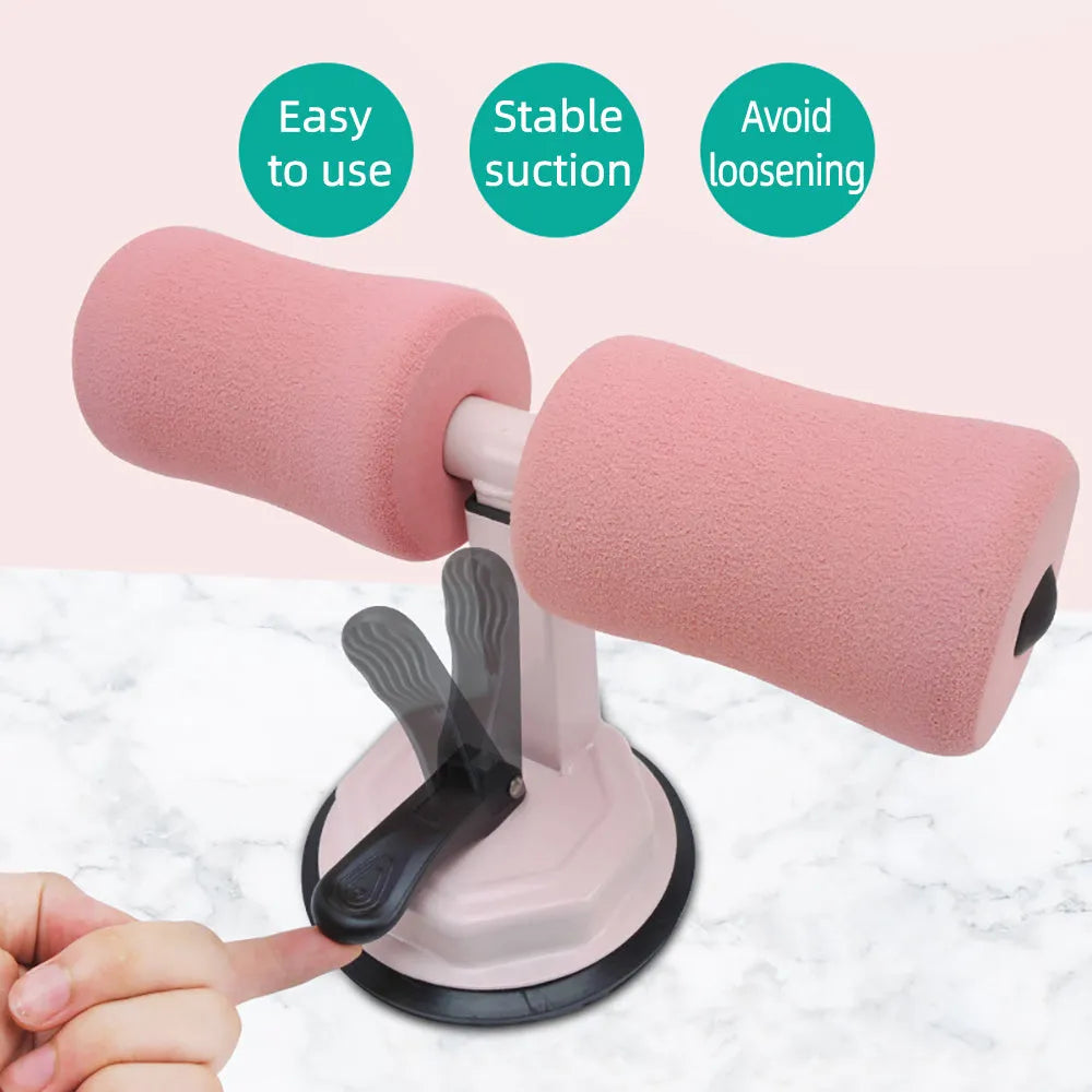 Pink adjustable sit-up bar with foam handles and suction base on a smooth floor for home fitness