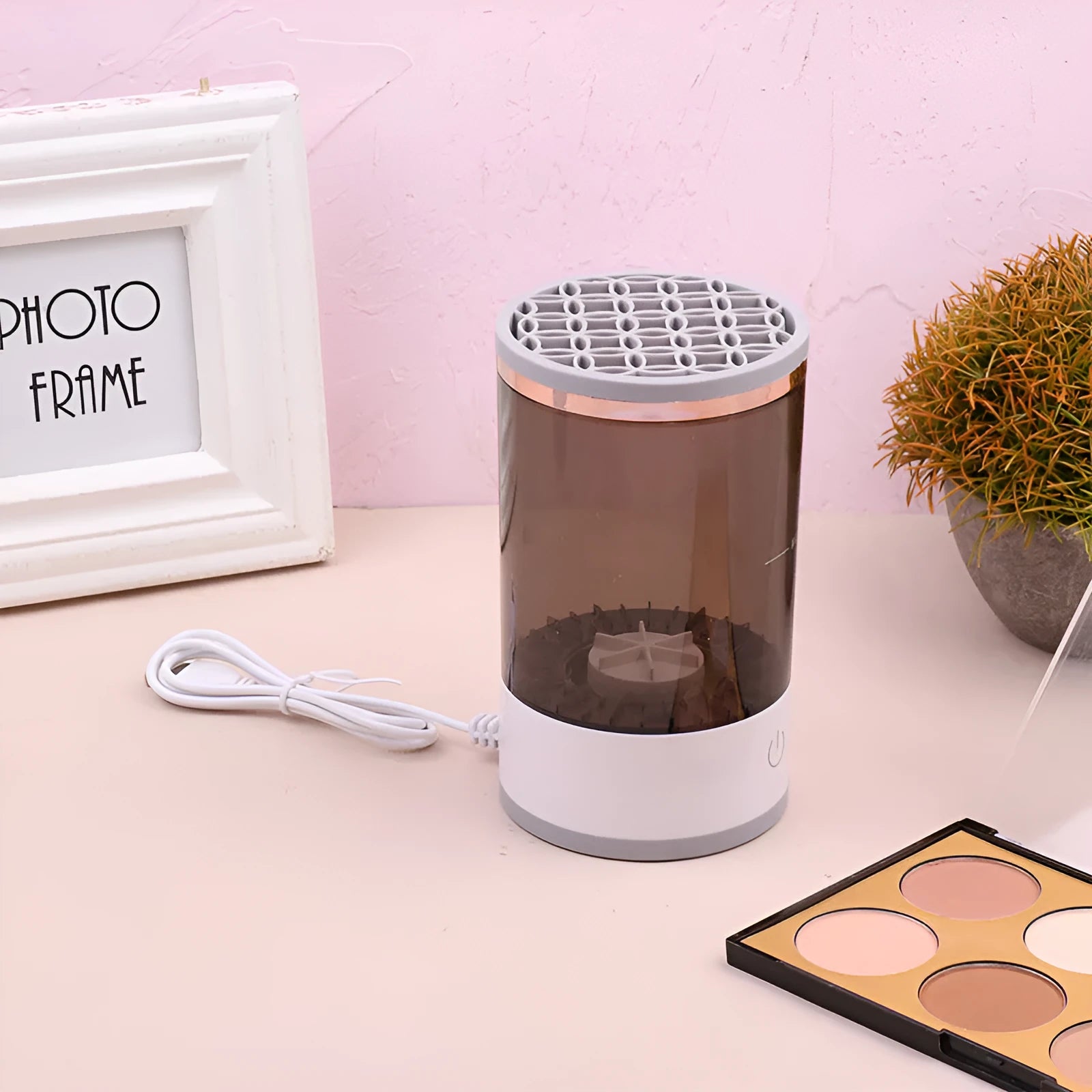 Grey and white electric makeup brush cleaner with USB charging cable on a wooden surface