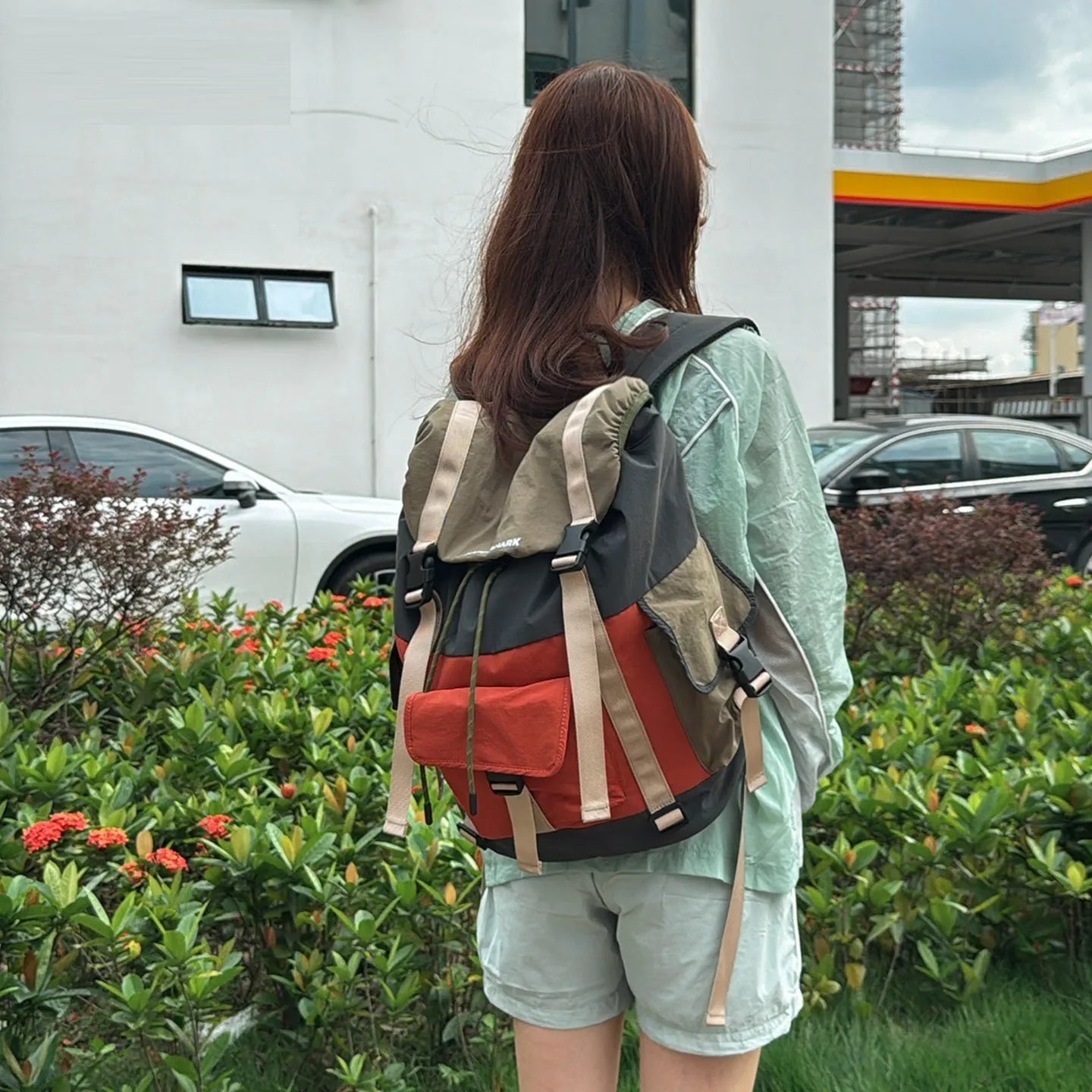 Orange and green contrast colour large outdoor backpack with multiple compartments on a neutral background.
