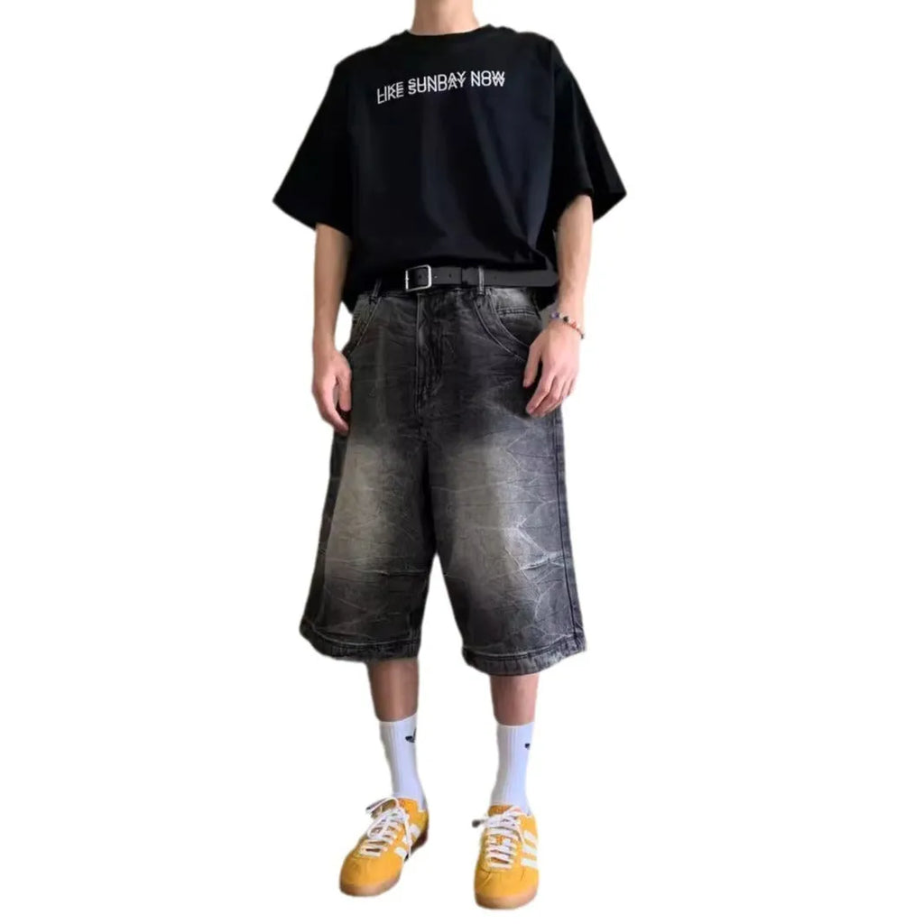 Man wearing loose straight-leg washed denim shorts in blue, showing cropped length and casual style.