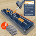 Large flat mop with long stainless steel handle, blue rotating head, and integrated scraper on a hardwood floor.