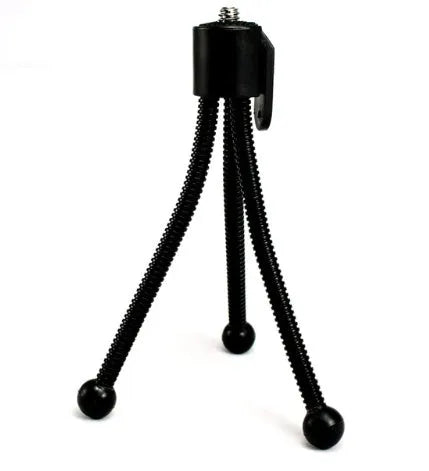Compact silver metal mini tripod with ball head, shown folded next to an iPhone for scale.