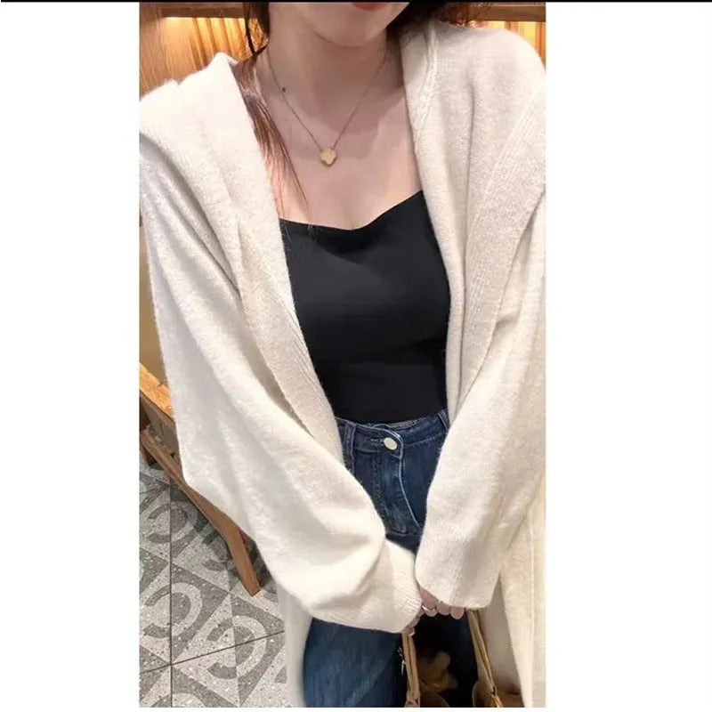 A woman wearing a long, beige, hooded knitted cardigan with a loose fit and below-the-knee length.
